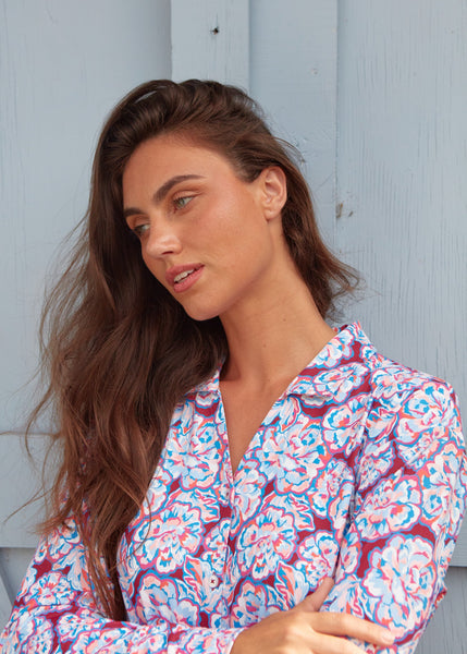A close up of a brunette woman looking to the side wearing the sun protective Cabana Life Camden Peony Button Down Shirt Dress with her arms crossed.