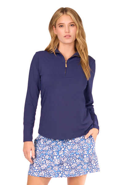A blonde woman wearing the sun protective Navy 1/4 Zip Sport Top and navy floral patterned Seaside 17" Skort from Cabana Life on a white background.
