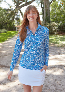 A redhead wearing the sun protective & navy Seaside Floral 1/4 Zip Sport Top and White 14" Skort from Cabana Life in front of trees and a dirt path.