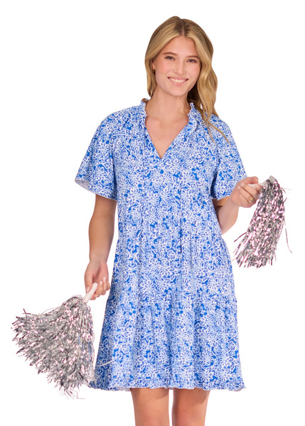 A blonde woman holding silver pom poms and wearing the sun protective Blue Short Sleeve Tiered Dress from Cabana Life on a white background.
